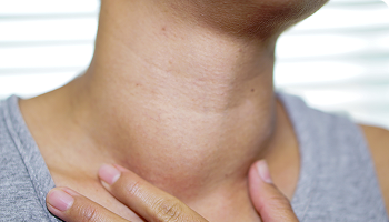 Close-up of a person's neck with their hand resting on their throat, possibly indicating throat diswelling
